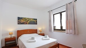 Un dormitorio con una cama de madera, dos mesitas de noche con lámparas, una ventana con cortinas y un cuadro de un cactus en la pared.