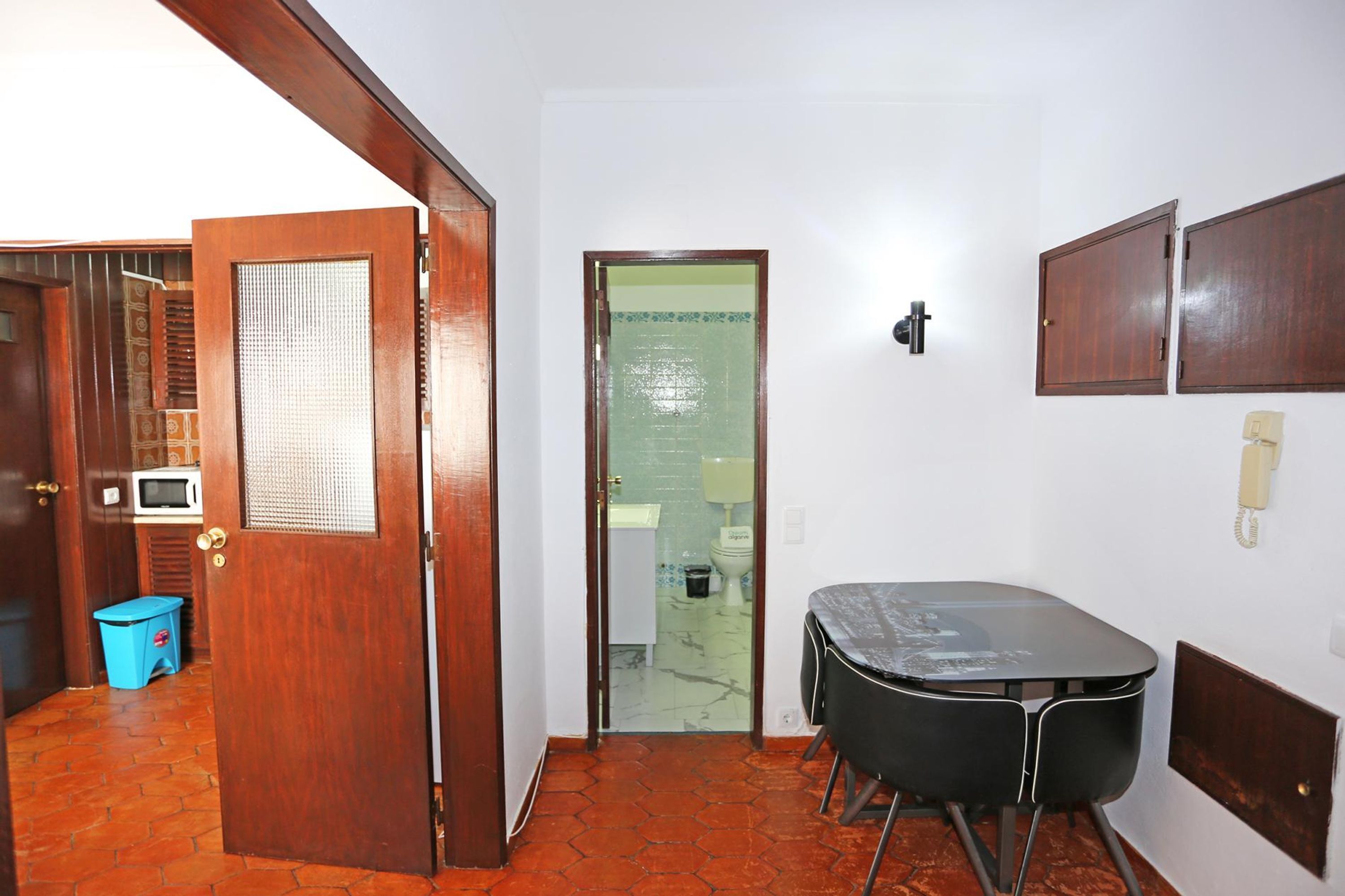 A room with a wooden door, a small table with chairs, a telephone, and a microwave in the background.