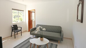 Ein Wohnzimmer mit grauem Sofa, einem schwarzen Sessel, einem kleinen weißen Tisch und einer Topfpflanze.