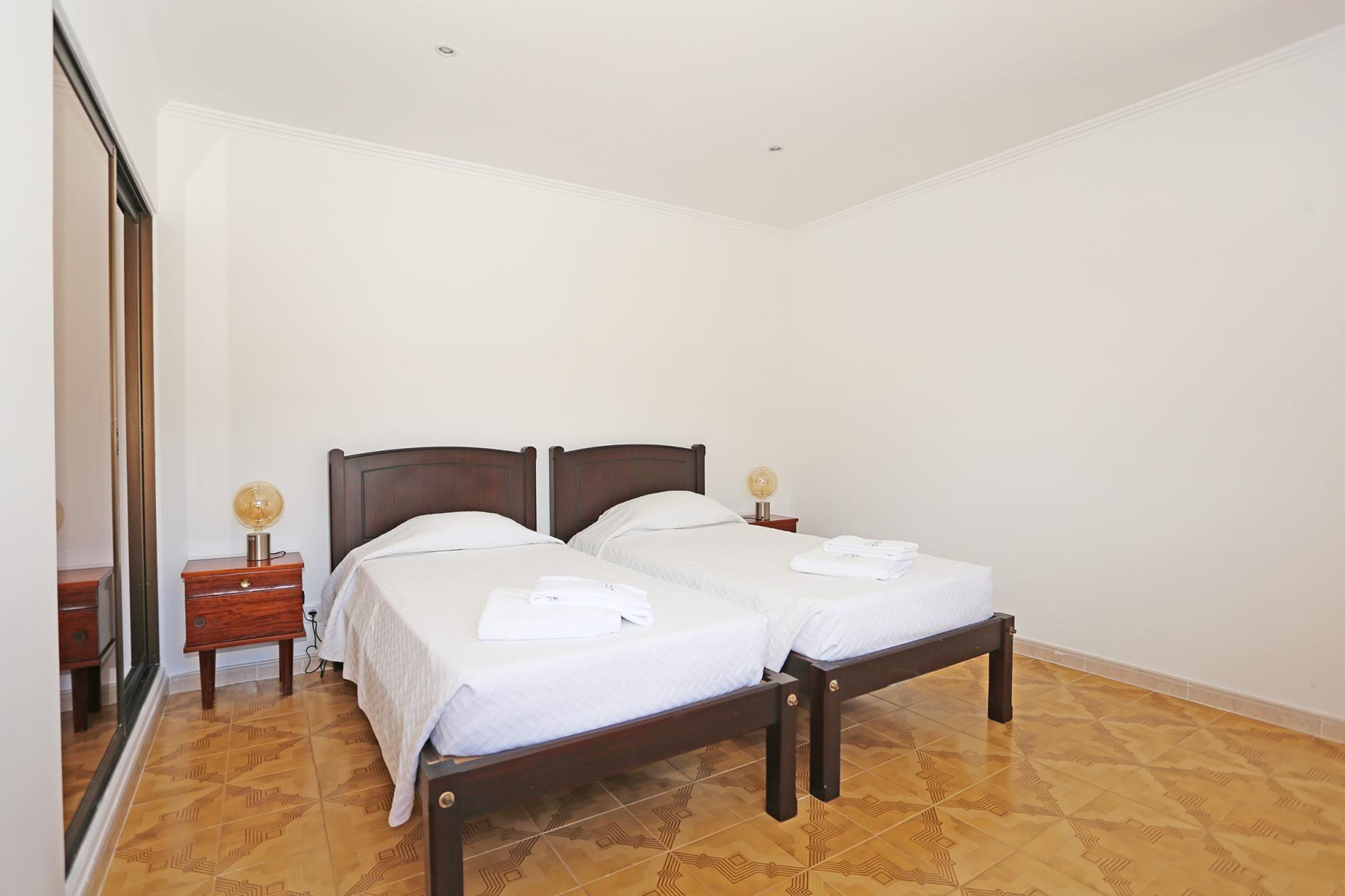 A double bed with wooden headboards, a bedside table with a lamp, and a mirror on the left wall.