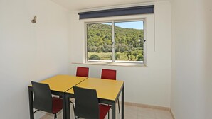 Ein Zimmer mit einem gelben Tisch, vier Stühlen, einem Fenster mit Blick auf eine grüne Landschaft und weißen Wänden.