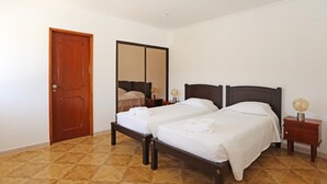 Ein Schlafzimmer mit zwei Einzelbetten, einer Holztür, einem großen Spiegel und einem Nachttisch mit Lampe.