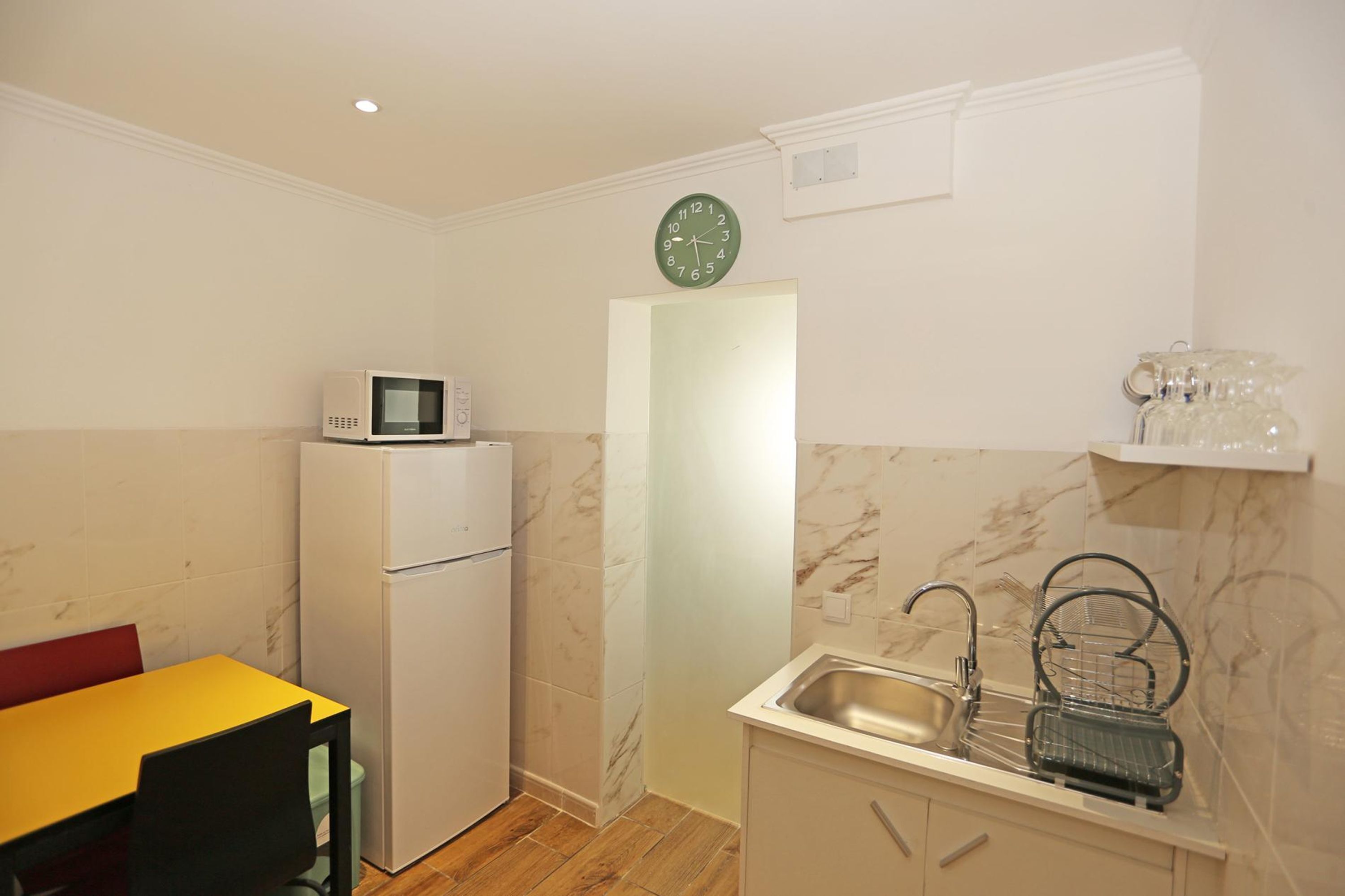 A compact kitchen with a microwave, refrigerator, sink, and a clock on the wall.