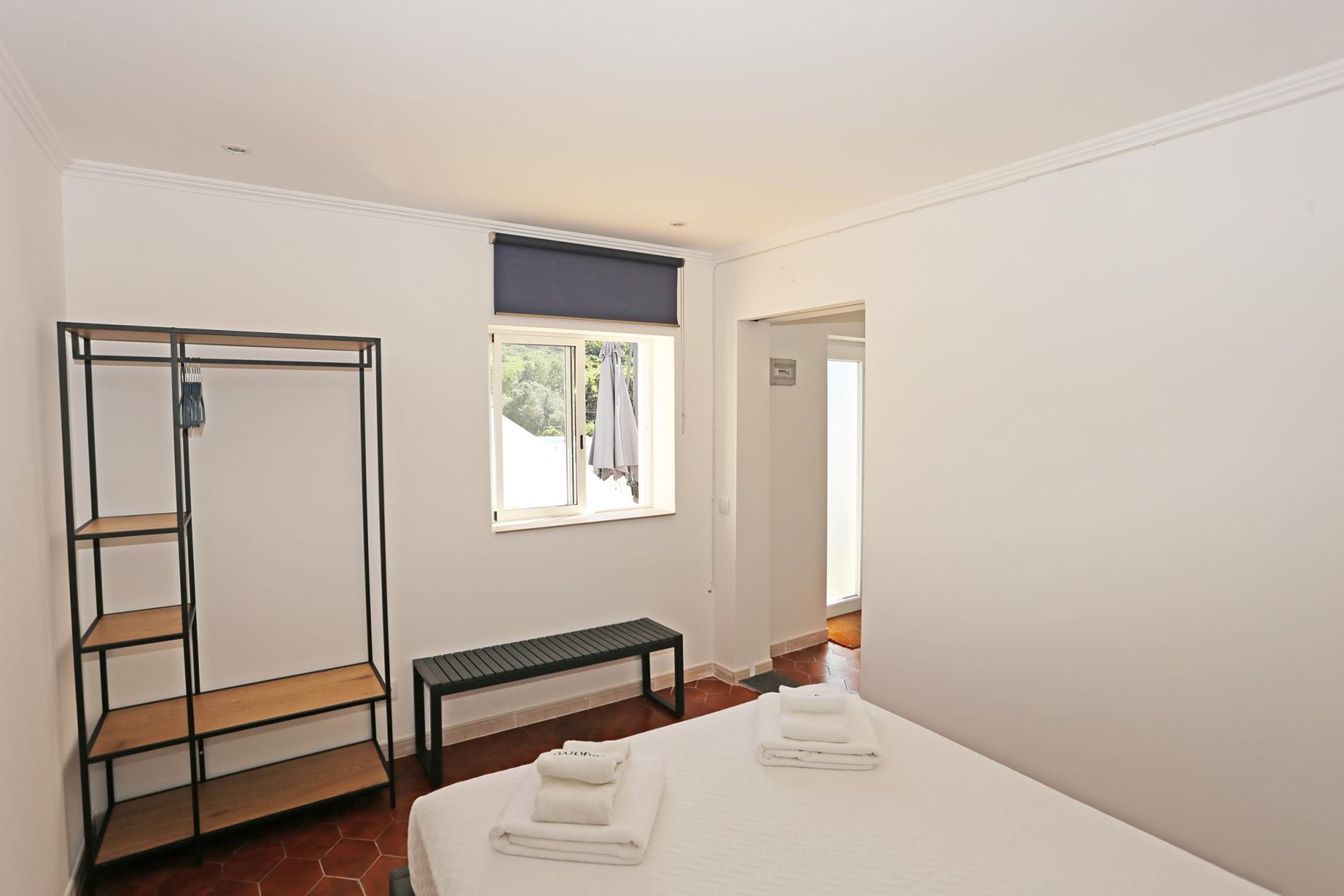 A bedroom with a bed, a bench, a wardrobe, and a window with a view of the outside.