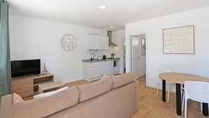 A modern living room with a sofa, TV, and dining area with chairs. - X 05 - 1 Bed Apartment in Quinta da Ponte (Lagos)