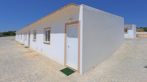 A row of white buildings with a tiled roof, a door labeled '5', and a small green mat at the entrance. - X 05 - 1 Bed Apartment in Quinta da Ponte (Lagos)