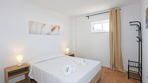 Habitación de hotel ordenada con cama, lámparas de noche, ventana con cortinas, un perchero y una obra de arte colgada en la pared.