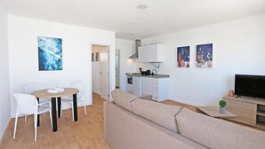 Una sala moderna con sofá, una mesa de comedor con sillas, una zona de cocina y un televisor sobre un mueble de madera.