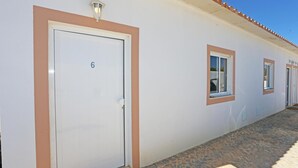 A building with a white exterior, numbered room 6, and a tiled ground. - X 06 - 1 Bed Apartment in Quinta da Ponte (Lagos)