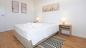 A bedroom with a bed, two bedside lamps, a small wooden nightstand, a patterned rug, and two framed pictures on the wall. - X 10 - 2 Bed Apartment in Quinta da Ponte (Lagos)