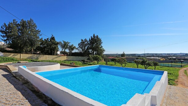A rectangular swimming pool with a white border, surrounded by a paved area and greenery. - X 10 - 2 Bed Apartment in Quinta da Ponte (Lagos)