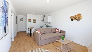 A modern living room with a sofa, a small table, and a kitchen in the background. - X 10 - 2 Bed Apartment in Quinta da Ponte (Lagos)