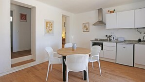 A modern kitchen with white cabinets, a built-in oven, and a sink. There is a dining area with a round wooden table and white chairs. - X 01 - 2 Bed Apartment in Quinta da Ponte (Lagos)