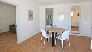 A dining area with a round wooden table and four white chairs, a sofa in the background, and a framed picture on the wall. - X 01 - 2 Bed Apartment in Quinta da Ponte (Lagos)