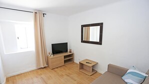 A modern living room with a wooden floor, a beige sofa, a TV on a wooden stand, and a small table with a remote control. - X 01 - 2 Bed Apartment in Quinta da Ponte (Lagos)