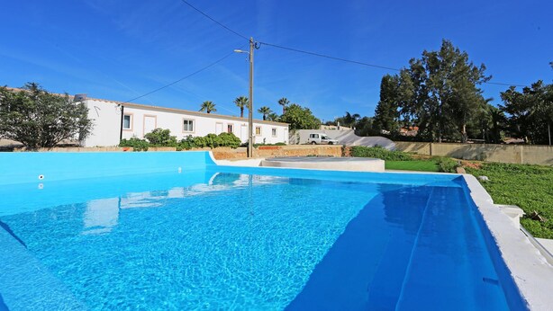 A swimming pool with a clear blue water surface, surrounded by a white pool deck and a grassy area. - X 01 - 2 Bed Apartment in Quinta da Ponte (Lagos)