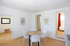 A room with a round wooden table surrounded by four white chairs, a wooden bench, and a framed picture on the wall. - X 01 - 2 Bed Apartment in Quinta da Ponte (Lagos)