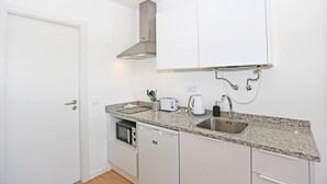 A compact kitchen with white cabinets, a granite countertop, a built-in oven, a dishwasher, and a stainless steel sink. - X 04 - 1 Bed Apartment in Quinta da Ponte (Lagos)