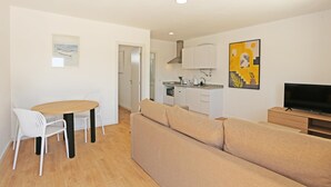 A modern living room with a sofa, a dining table with chairs, a kitchen area, and a TV. - X 04 - 1 Bed Apartment in Quinta da Ponte (Lagos)