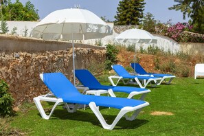 Outdoor lounge chairs with white umbrellas, arranged on a grassy area with a stone wall and vegetation in the background. - X 03 - 1 Bed Apartment in Quinta da Ponte (Lagos)
