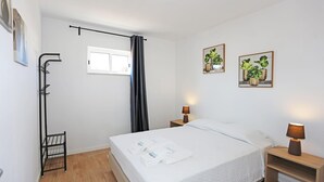 Een keurig opgemaakte slaapkamer met een bed, nachtlampjes, een raam met gordijnen en twee plantenfoto's aan de muur.