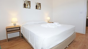A neatly made bed with white linens and two bedside lamps, a wooden nightstand, and two wall-mounted paintings. - X 09 - 1 Bed Apartment in Quinta da Ponte (Lagos)