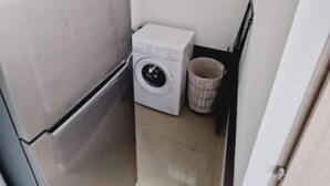 A compact kitchen with a refrigerator, a washing machine, and a small trash bin. - Quiet, fully-equipped house with garden (Maing)