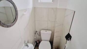 Une petite salle de bain compacte, équipée de toilettes, d’un lavabo et d’un miroir.