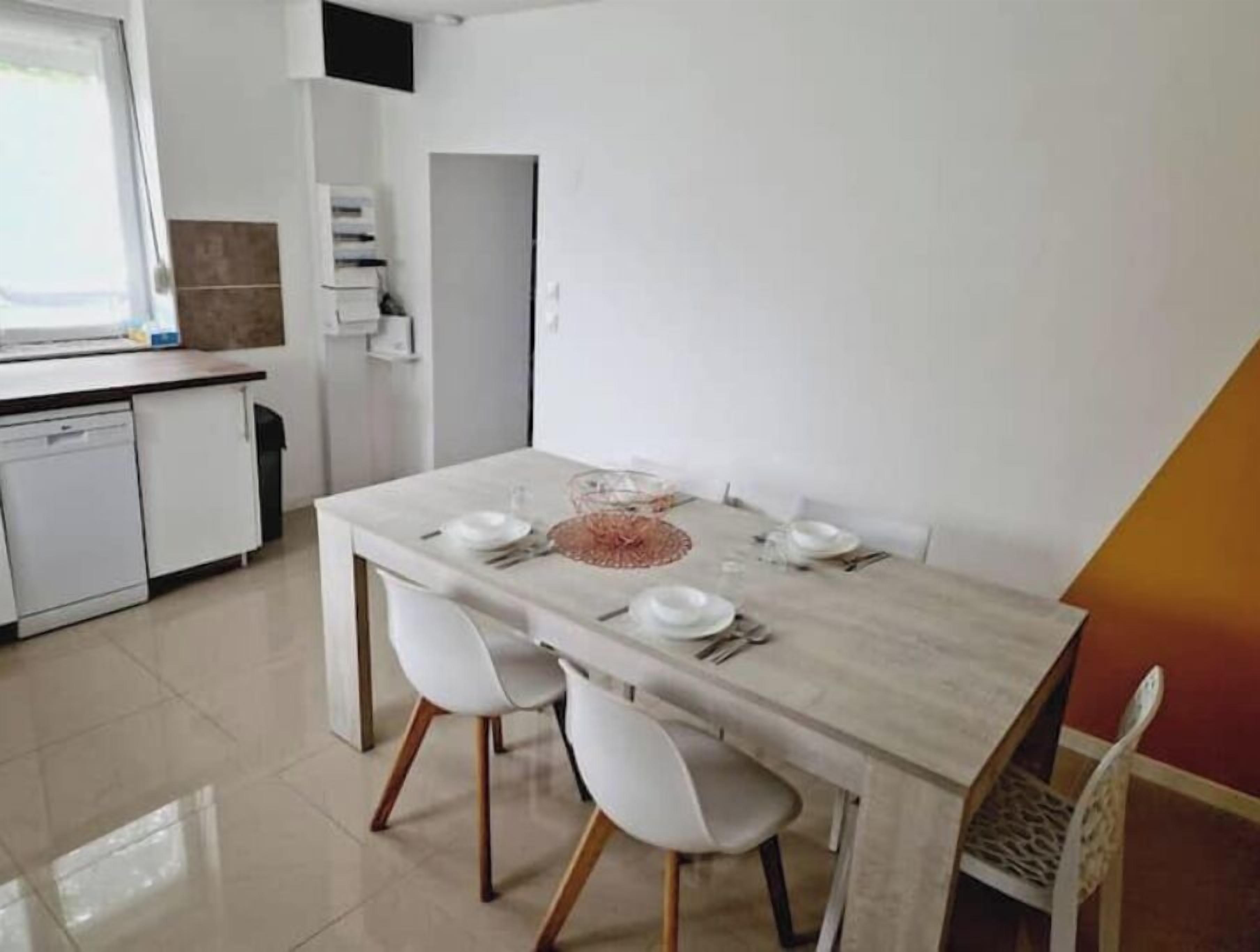 Een eetruimte met een marmeren tafel voor vier personen, witte stoelen en een keuken met witte kasten en een vaatwasser.