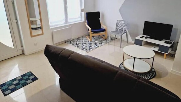 A modern living room with a sofa, a TV, a small table, and a patterned rug. - Quiet, fully-equipped house with garden (Maing)