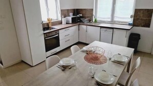 A modern kitchen with white cabinets, a dining table set for four, and a window providing natural light. - Quiet, fully-equipped house with garden (Maing)