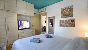 Une chambre d’hôtel avec un lit, un téléviseur posé sur une commode, une armoire et deux œuvres d’art accrochées au mur.