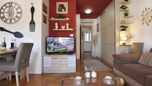 Un salon avec un téléviseur, un coin repas avec une table et des chaises, un canapé et des objets décoratifs disposés sur des étagères.