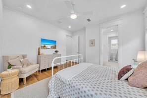 A bedroom with a bed, a dresser, a chair, a small table, and a ceiling fan.