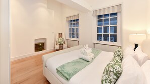 Quarto com cama grande, lareira, poltrona e duas janelas.