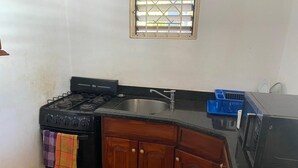 A compact kitchen with a gas stove, a sink, wooden cabinets, and a microwave.