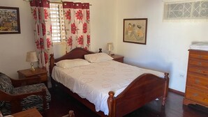 A bedroom with a wooden bed, a chair, a dresser, and two paintings on the walls.
