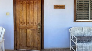 A wooden door with a metal handle, a wicker chair, and a wall-mounted light fixture.