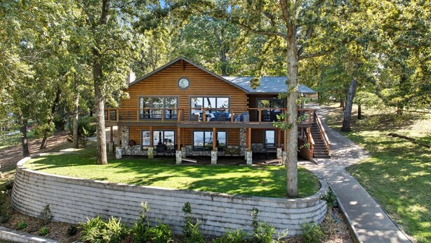 A two-story log cabin with a stone foundation, a deck, and a staircase leading to the upper level. - Lakefront Luxury Log Cabin on Grand Lake O’ the Cherokees (Jay)