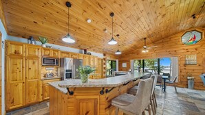 A wooden cabin-style kitchen with a large island, bar stools, and a view of the outdoors. - Lakefront Luxury Log Cabin on Grand Lake O’ the Cherokees (Jay)