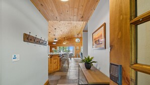 A hallway with wooden ceiling and walls, a potted plant on a bench, a door with a keypad lock, and a wall-mounted coat rack. - Lakefront Luxury Log Cabin on Grand Lake O’ the Cherokees (Jay)