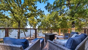 A wicker outdoor seating area with cushions, overlooking a body of water. - Lakefront Luxury Log Cabin on Grand Lake O’ the Cherokees (Jay)