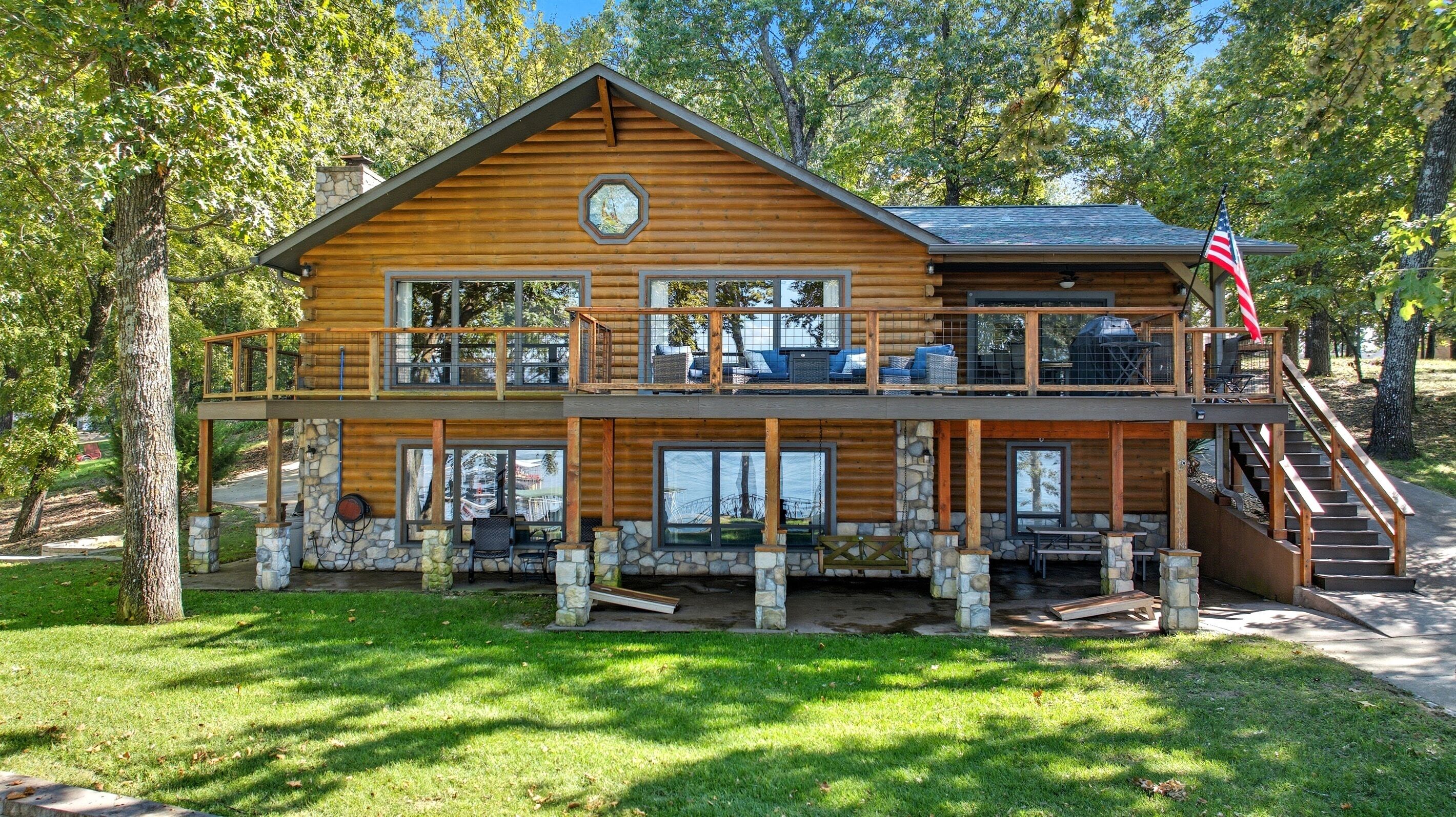 A two-story log cabin with a balcony, stone foundation, and a flag.
