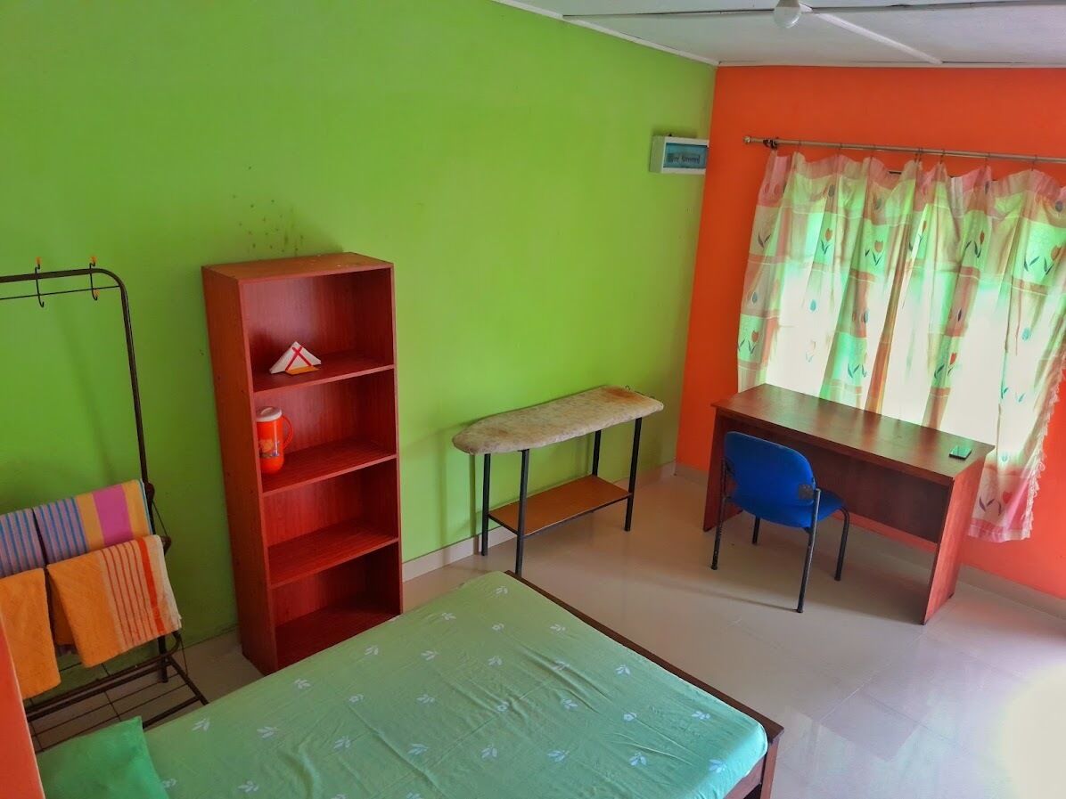 Une pièce comprenant un lit, un bureau, une chaise, une bibliothèque et une fenêtre avec des rideaux.