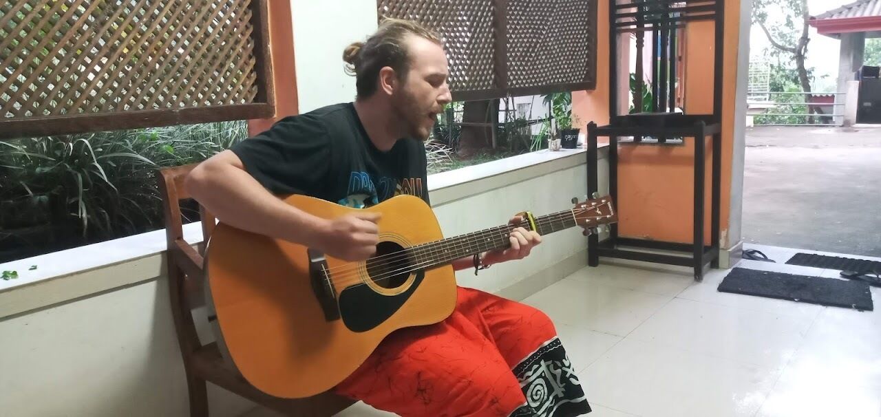 Iemand speelt op een akoestische gitaar in een ruimte met een raam en een deur op de achtergrond.