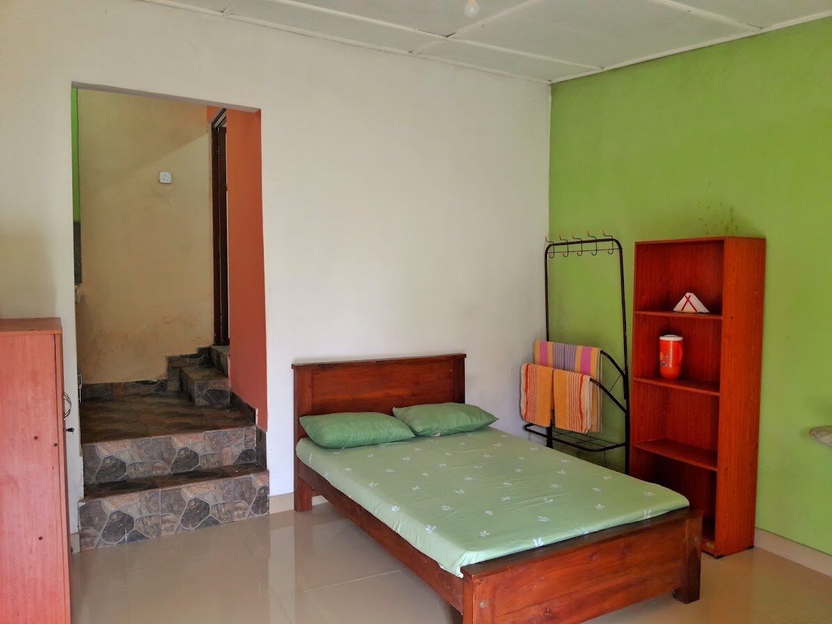 Een slaapkamer met een bed, een houten garderobe, een plank met spullen en een trap naar een aangrenzende kamer.