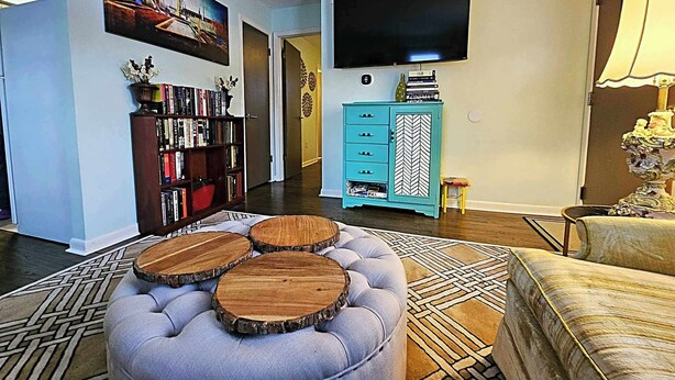 A living room with a large flat-screen TV, a bookshelf, a teal cabinet, and a patterned rug. - The Castro (Dayton)