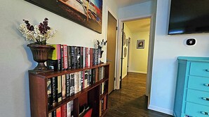 A hallway with a bookshelf filled with books, a painting on the wall, and a blue dresser. - The Castro (Dayton)
