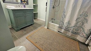 A bathroom with a vanity, a shower, and a patterned shower curtain. - The Castro (Dayton)