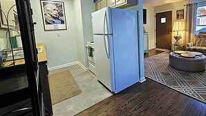 A compact kitchen with a refrigerator, a microwave, and a sink. There is a rug on the floor and a framed picture on the wall. - The Castro (Dayton)